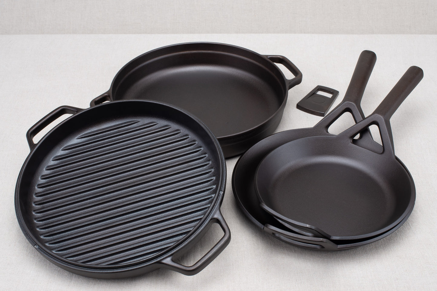 A set of black Borough Furnace cookware including a 10.5" frying skillet, a 9" frying skillet, a 12" braising skillet grill pan, and a braising lid with a bottle opener.